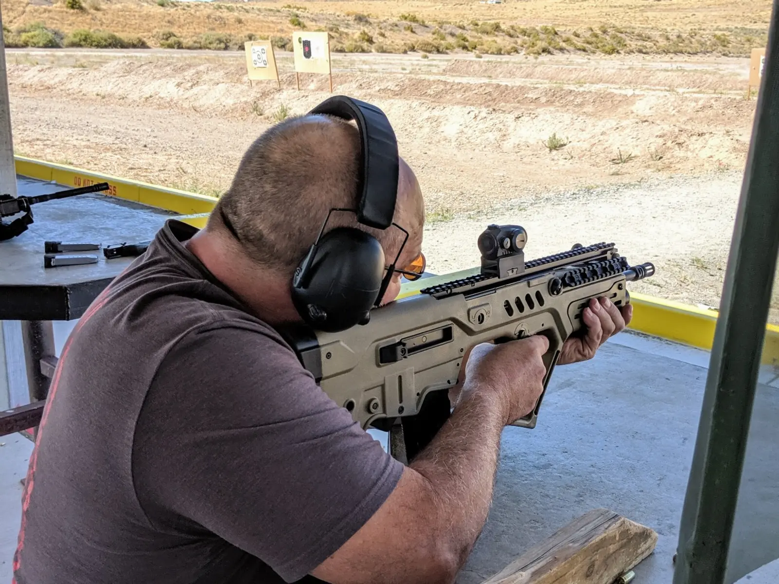 Shooter practicing with a Tavor bullpup rifle at an outdoor desert range