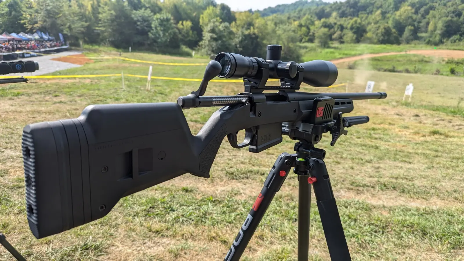 Precision bolt-action rifle supported on a tripod at an outdoor shooting range